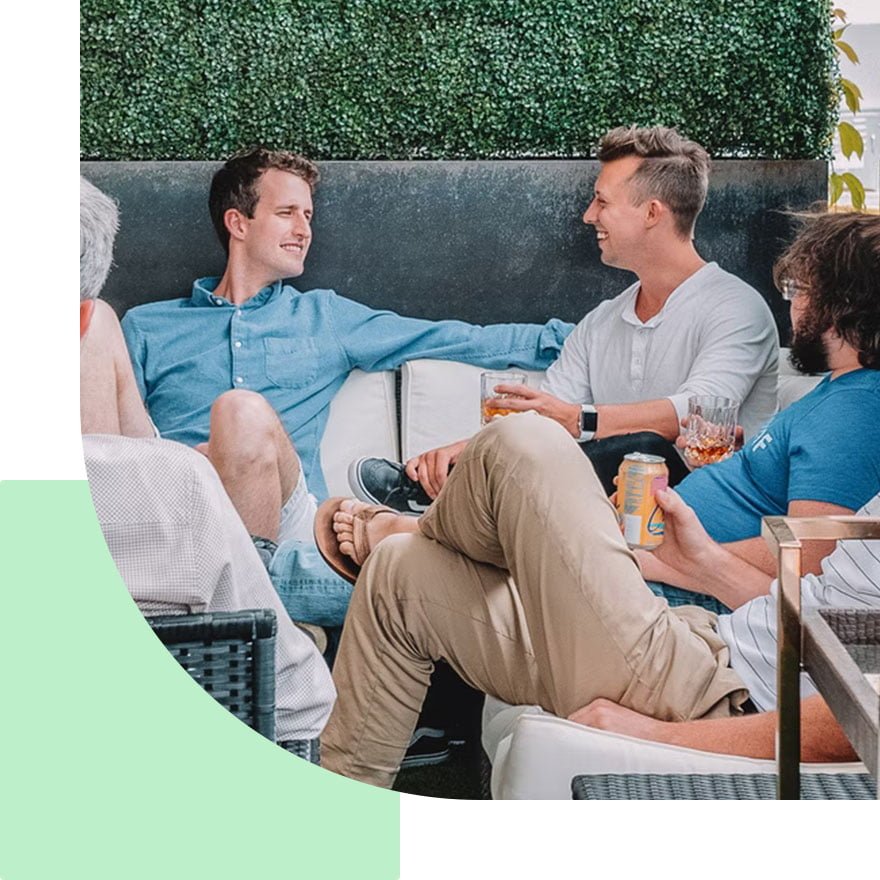 A group of friends enjoying a relaxed conversation outdoors with drinks in hand.
